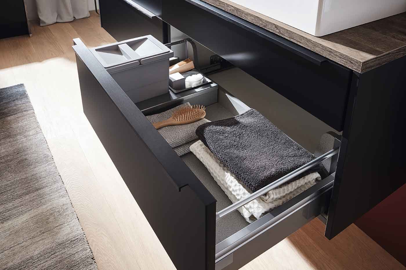 Der Inhalt einer schwarzen Schublade im Badezimmer mit Handtüchern un deiner Haarbürste