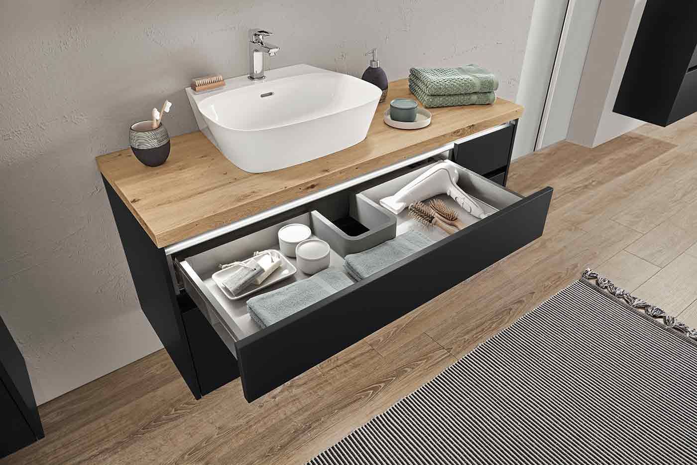 Unter einem Waschbecken geöffnete Schublade mit einem Haartrocker und Handtüchern