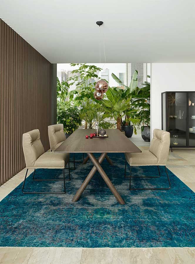 Esszimmer mit einem dunklen Holztisch und grauen Sesselstühlen auf einem petrolfarbenen Teppich 