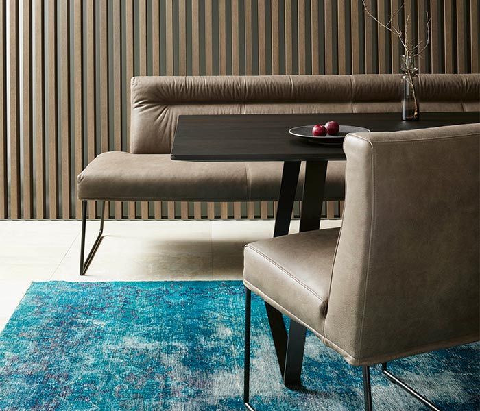 Schwarzer Esszimmertisch mit einer Ledersitzbank und Lederstuhl auf einem petrolfarbenden Teppich 