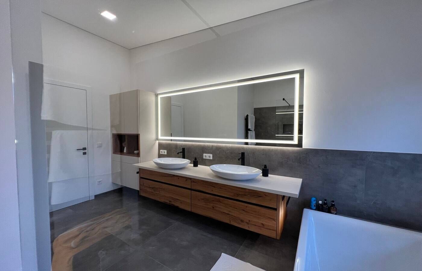 Waschbeckenschrank aus Hiólz mit zwei Waschbecken und einem beleuchteten Spiegel