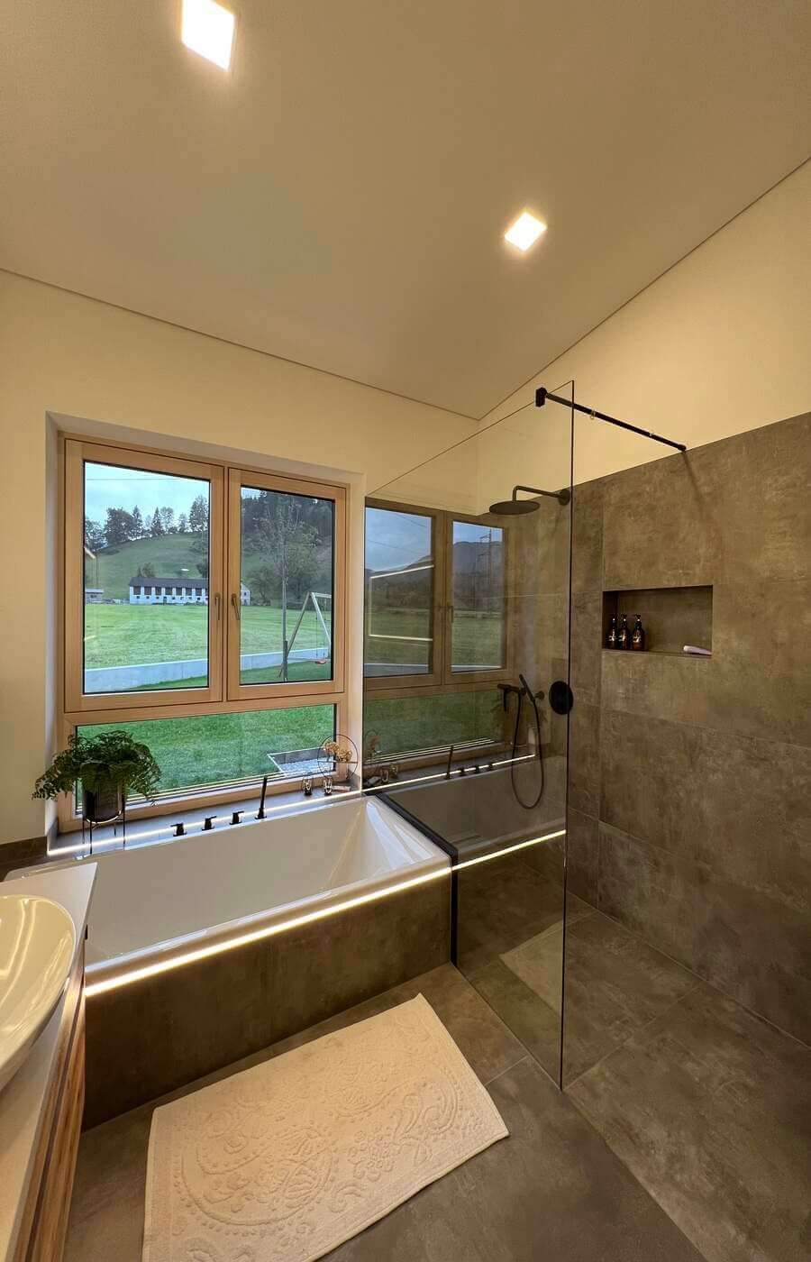 Große Dusche mit grauen Fliesen und einer beleuchteten Badewanne