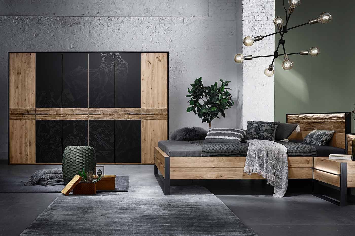 Bildergalerie Schlafzimmer Thiele Meyer Schlafzimmer mit einem Holzbett mit dunkelgrauer Bettwäsche und einem großen Holzschrank mit schwarzen Türen