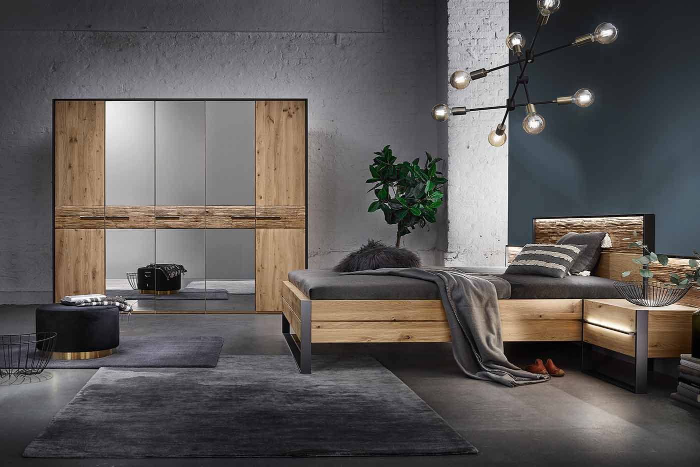 Schlafzimmer mit einem Holzbett mit dunkelgrauer Bettwäsche und einem großen Holzschrank mit schwarzen Türen