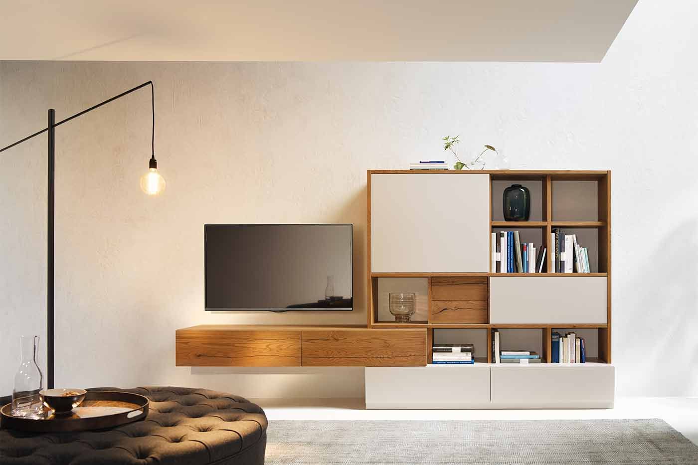 Bücherregal aus Holz und grauen Elementen mit einem angebundenen Sideboard über dem ein Fernseher hängt 